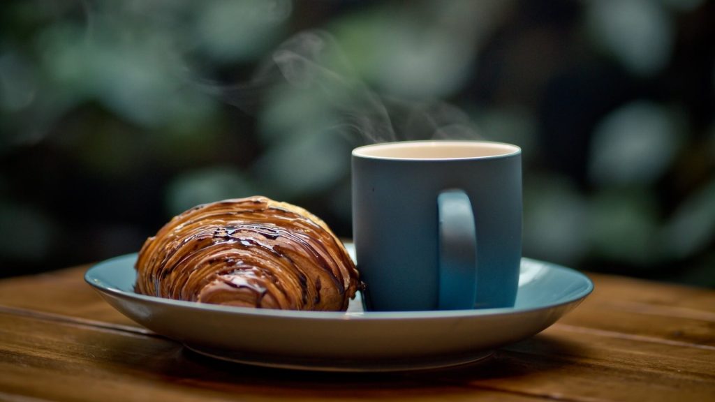 Eine frisch gebrühte Tasse Kaffee, serviert mit einem butterweichen Croissant, eine klassische Frühstückskombination.