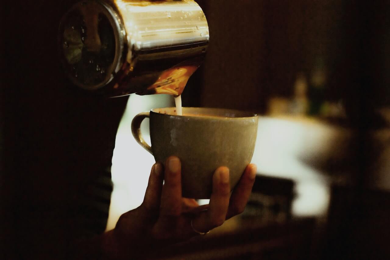 Ein erfahrener Barista gießt schaumige Milch in eine perfekt gebrühte Tasse Kaffee und kreiert so einen köstlichen Latte oder Cappuccino.